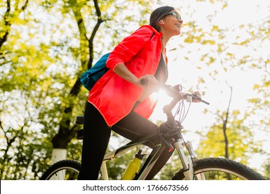 slim fit beautiful woman doing sports in morning in park riding on bicycle on road with yoga mat in colorful fitness outfit, exploring nature, smiling happy healthy lifestyle