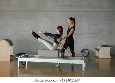 Slim fit Woman doing core exercises while taking Personal Pilates lesson on a Reformer machine, by a female instructor at a big gymnasium center, wide industrial studio. Healthy fitness lifestyle. - Powered by Shutterstock