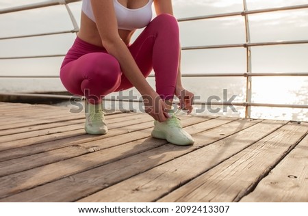 Slim fit woman tying the laces of sneakers on the beach. Healthy lifestyle. Outdoor workout
