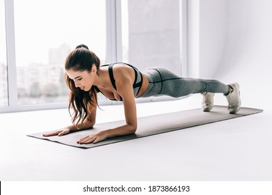 Slim fitnes young girl with ponytail doing planking exercise indoors at home gymnastics.