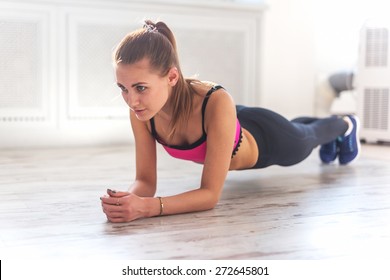 Slim fitnes young girl with ponytail doing planking exercise indoors at home gymnastics.