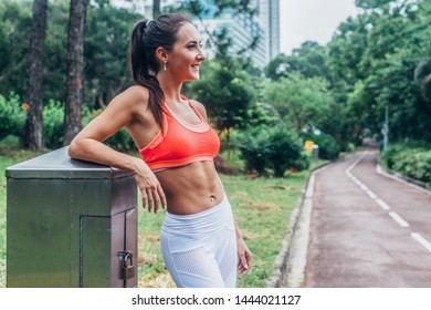 Slim Fitness Brunette Woman With Six Pack Abs Wearing Pink Sport Bra Standing In City Park Relaxing After Workout Looking Away From The Camera