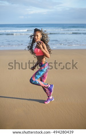 Slim fitness woman with earphones running at the beach. Black female athlete exercising outdoor near the sea.