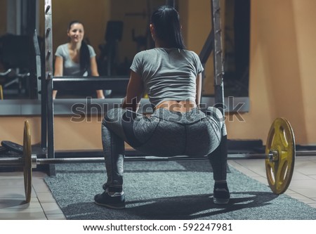 Slim girl bodybuilder lifting heavy barbell standing in front of the mirror while training in the gym. Sports concept, fat burning and a healthy lifestyle.