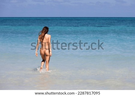 Slim girl with long hair wearing bikini running to swim in blue sea water. Beach vacation on Caribbean islands