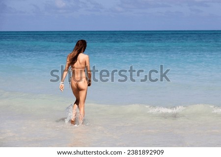 Slim girl with long hair wearing bikini running to swim in blue sea water. Beach vacation on tropical islands