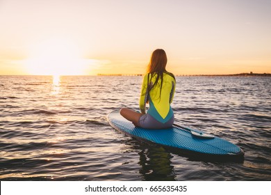 Slim girl on stand up paddle board on a quiet sea with summer sunset colors. Relaxing in ocean