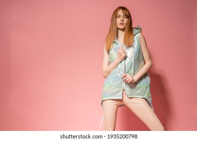 Slim girl with red hair in modern clothing posing in front of pink background