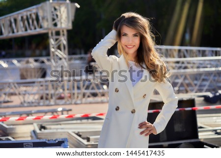 slim girl in a white coat  standing next to a flightcase with concert equipment. Preparing the stage for a concert in the open air.