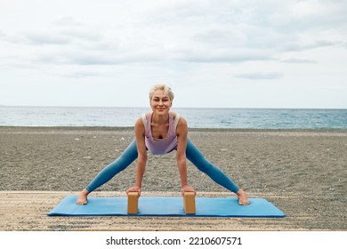 Slim Good Looking Woman Practicing Yoga At The Beach Using Wooden Yoga Blocks For More Comfortable And Easier For Practise While Doing Exercise.