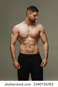 Slim muscular male model at gray background. Fitness shirtless guy in black sport pants posing in studio. - Shutterstock ID 2340718783