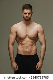 Slim muscular male model at gray background. Fitness shirtless guy in black sport pants posing in studio. - Shutterstock ID 2340718785