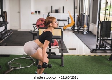 A Slim And Sexy Asian Woman Does Regular Dumbbell Squats At The Gym. Leg Workout. Side View.