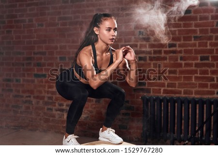 Slim sport woman in sportswear jumping on fit box and do squats. bodybuilding. Brickwall background