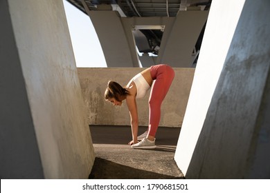 Slim Sportswoman In Pink Legging Standing Under The Bridge, Stretching Muscles Making Functional Training, Makes A Slope Before A Work Out And Jogging. Spine, Hamstring Stretch. 