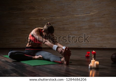 Slim sporty woman stretching her legs on the yoga mat and bending her back while touching the toes