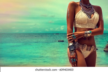 Slim and tanned girl in trendy Boho style on the beach. Girl in a white knit swimsuit with silver jewelry . Bracelets and rings with turquoise stones.