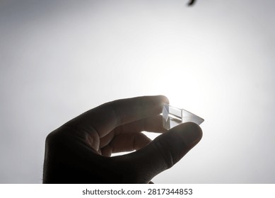 Slim triangular glass prism held at arm length near the sun shows subtle internal reflections and experimentation vibes great for lessons about refraction creativity and simple scientific play