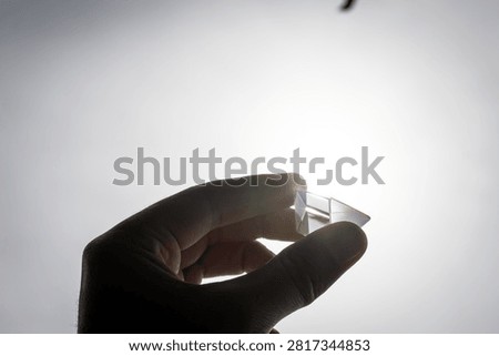 Slim triangular glass prism held at arm length near the sun shows subtle internal reflections and experimentation vibes great for lessons about refraction creativity and simple scientific play