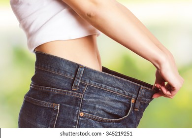 Slim Waist Of Young Woman With Perfect Healthy Thin Body,showing Her Old Jeans After Successful Diet. .Weight Loss And Slimming Concept.