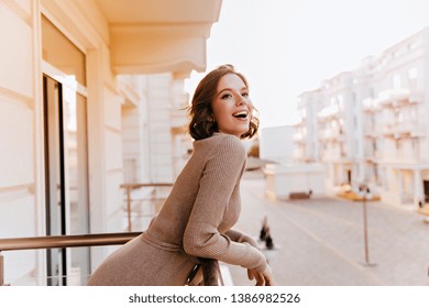 Slim well-dressed girl looking at city from balcony. Attractive sensual woman enjoying town view while standing at terrace.