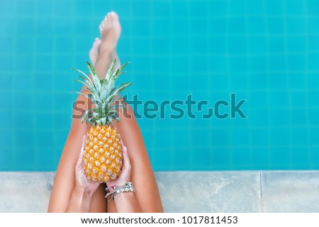 Slim woman holding pineapple fruit near swimming pool tropical exotic concept top view