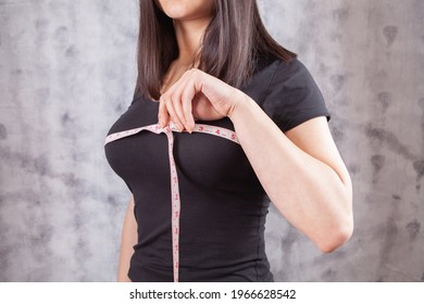 Slim woman measures her breast with a measuring tape