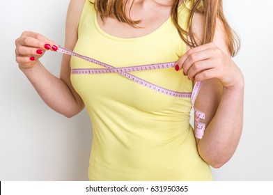 Slim woman measures her breast with a measuring tape - isolated on white