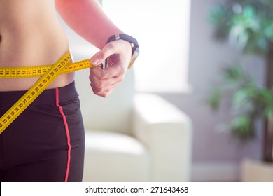 Slim woman measuring waist with tape measure at home in the living-room
