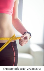 Slim Woman Measuring Waist With Tape Measure At Home In The Living-room