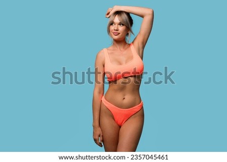 Slim woman posing in an orange swimsuit on a blue background. Healthy slender girl shows epilation or depilation of armpits, smooth healthy skin without damage and irritation 