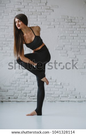 Slim woman practices yoga in white backlit studio