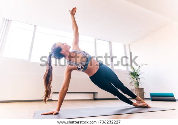 Slim woman\
in side plank pose at yoga class, Vasisthasana exercise. Female\
balancing on mat indoors at fitness\
gym