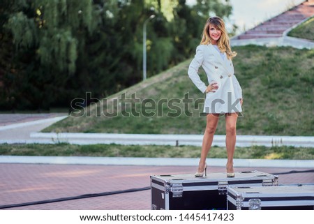 slim woman in a white coat  standing next to a flightcase with equipment. Preparing the stage for a concert in the open air. copy space