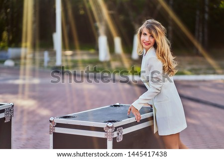 slim woman in a white coat standing next to a flightcase with equipment. Preparing the stage for a concert in the open air. copy space