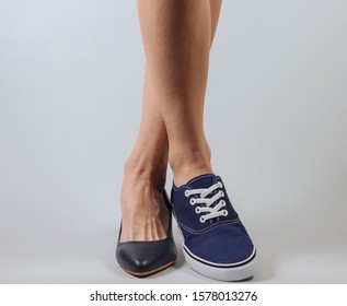 Slim Woman's Legs In Two Different Shoes With Heels And Sneakers On White Background. Creative Fashion Shot