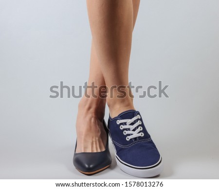 Slim woman's legs in two different shoes with heels and sneakers on white background. Creative fashion shot