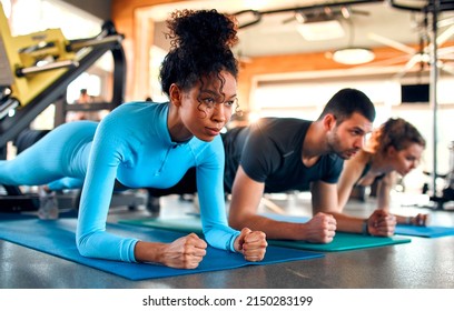 Slim women african american and caucasian ethnicity and muscular man in sportswear doing plank exercise on rubber mat in gym club. The concept of sports and recreation. - Powered by Shutterstock