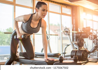 Slim young beautiful girl warming up with weights in health club.