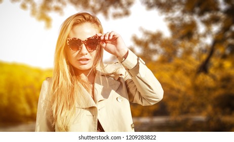Slim young blond woman with sunglasses and autumn background of lake. Sunset time and blurred background. 