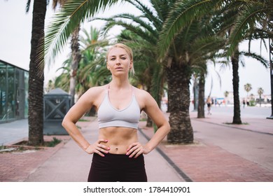 Slim Young Confident Female Athlete In Trendy Sportswear Standing With Hands On Waist On Street In Tropical City And Looking At Camera