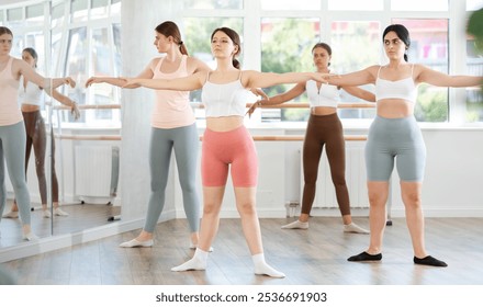 Slim young girl practicing ballet positions standing in row with others during workout session - Powered by Shutterstock