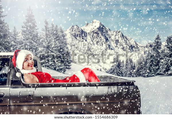 Slim young Santa Claus woman,white winter car with\
christmas gifts.Free space for your decoration.Snowflakes and\
landscape of mountains and forest of frost.Copy space.Xmas time and\
cold december day.