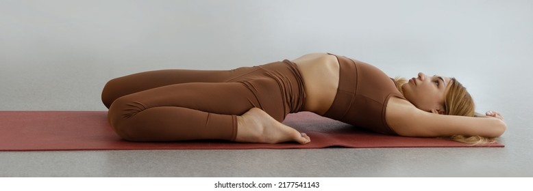 Slim young woman lying in Supta Virasana, reclining Hero Pose, stretching abdominal and back muscles on mat in gym - Powered by Shutterstock