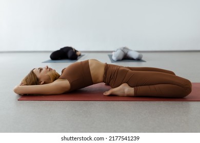 Slim young woman lying in Supta Virasana, reclining Hero Pose, stretching abdominal and back muscles on mat in gym - Powered by Shutterstock