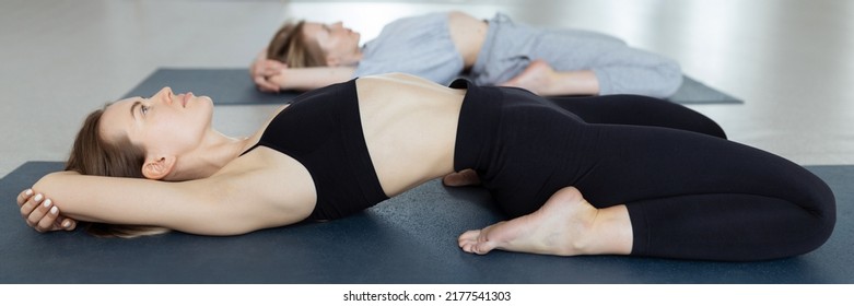 Slim young woman lying in Supta Virasana, reclining Hero Pose, stretching abdominal and back muscles on mat in gym - Powered by Shutterstock