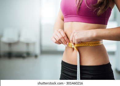 Slim young woman measuring her thin waist with a tape measure, close up
