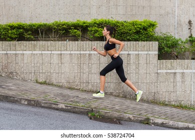 Slim Young Woman Running Uphill On Sidewalk Of City Street. Female Athlete Training Outside