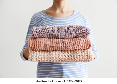 Slim Young Woman Wearing Oversized Cotton Shirt With Blue Stripes & Holding Big Stack Of Folded Knitted Warm Pastel Color Sweaters, Easy Chic Style, Different Knitting Patterns. Background, Copy Space