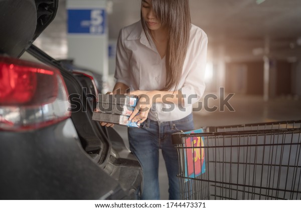 slime woman driver in motion of transfer\
loading goods daily products from the cart to back car storage\
after buy from\
supermarket